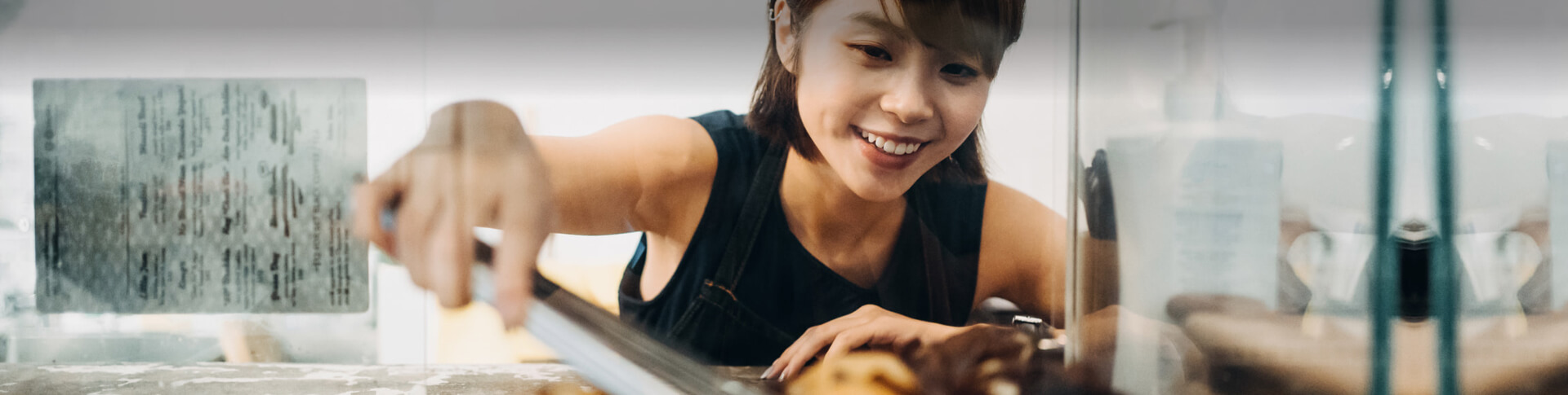 asiatische Frau mit Kuchenzange schaut in Vitrine
