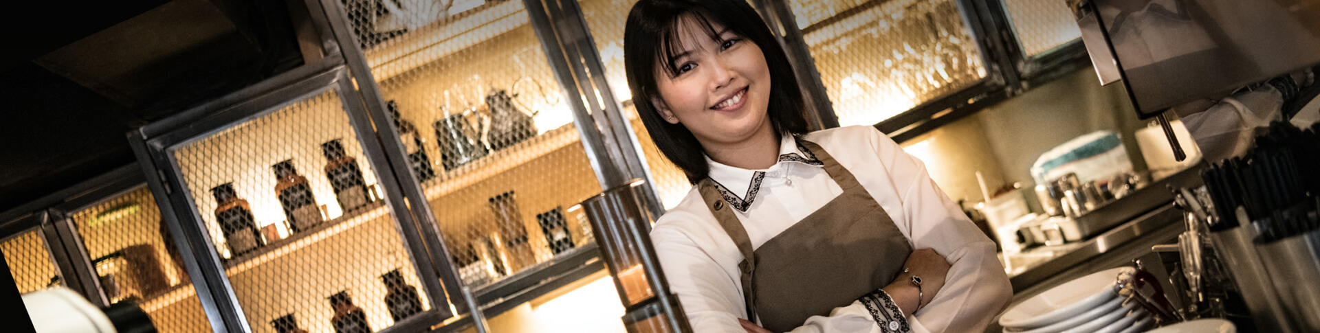 asiatische Frau mit Schürze hinter dem Tresen eines Kaffeehauses