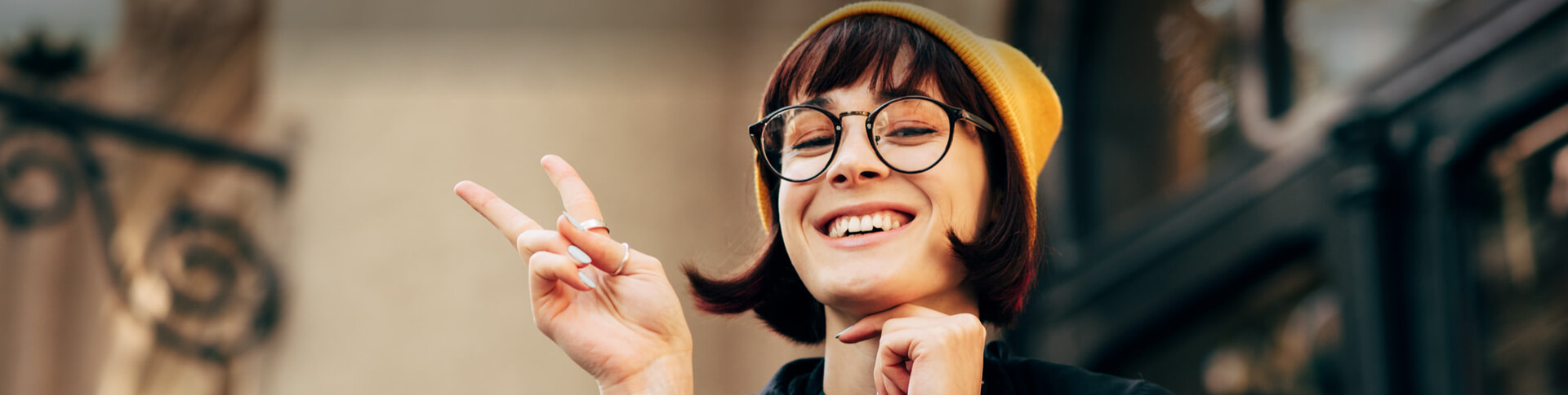 Frau mit Brille und gelber Mütze macht Peace-Zeichen