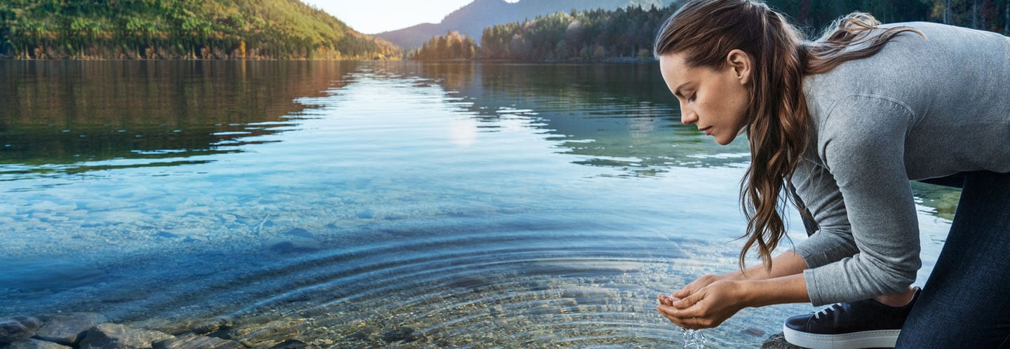 Frau schöpft mit den Händen Wasser aus einem See